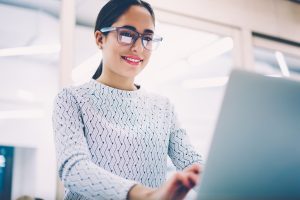 Positive female administrative manager typing feedback for clients comments on web pege working in clinic,smiling woman in spectacles making online research for report keyboarding on netbook